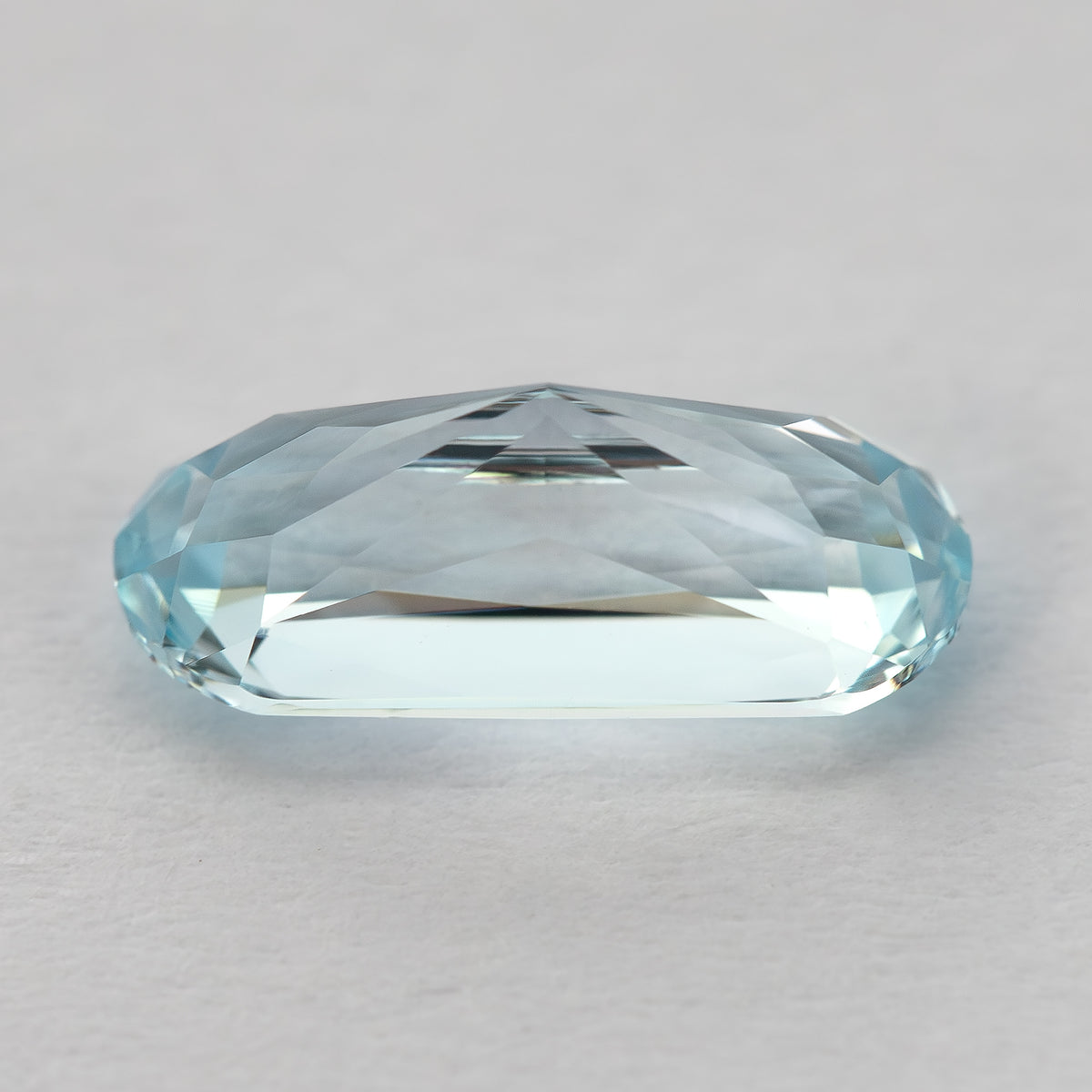 Side profile of the light blue sapphire on a pale surface, showing crown and pavilion depth.