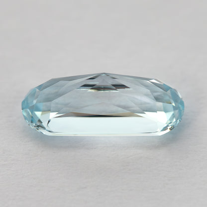 Side profile of the light blue sapphire on a pale surface, showing crown and pavilion depth.