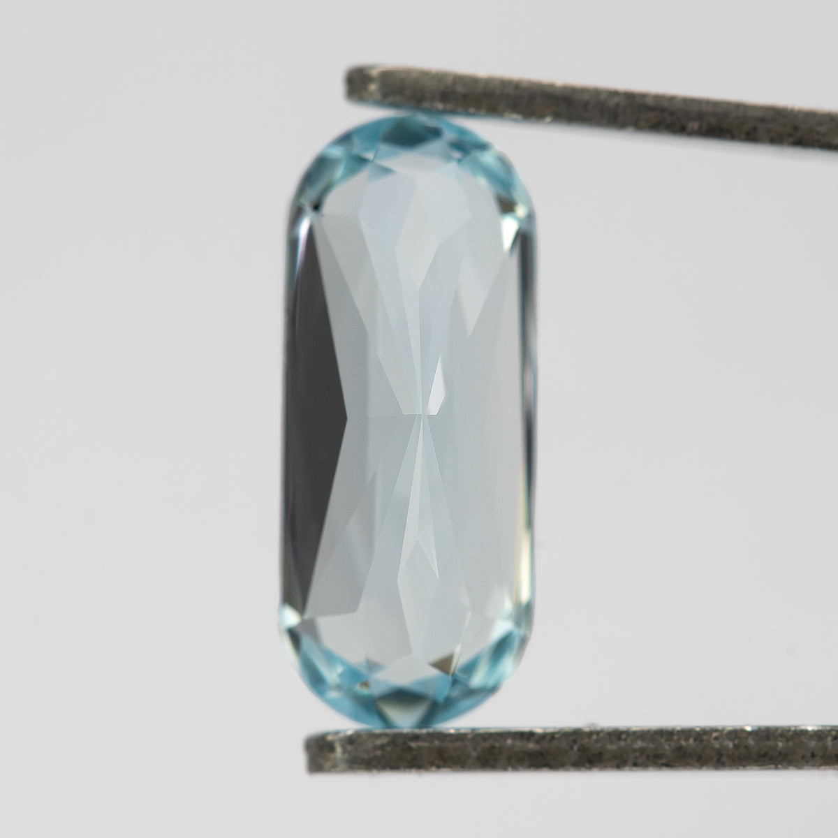 Reverse view of the long-oval sapphire held vertically in tweezers.