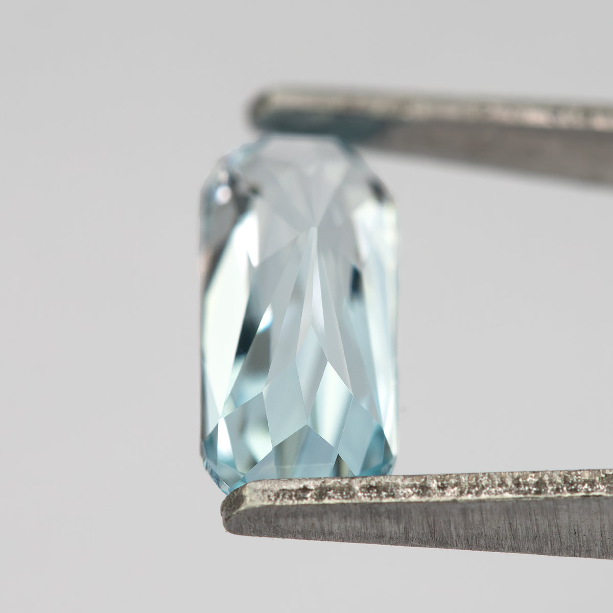 Oblique view of the sapphire in tweezers, showing thickness and side facets.