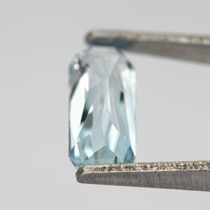Oblique view of the sapphire in tweezers, showing thickness and side facets.
