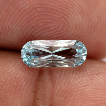 Elongated light blue sapphire resting across a fingertip, showing its rounded ends.