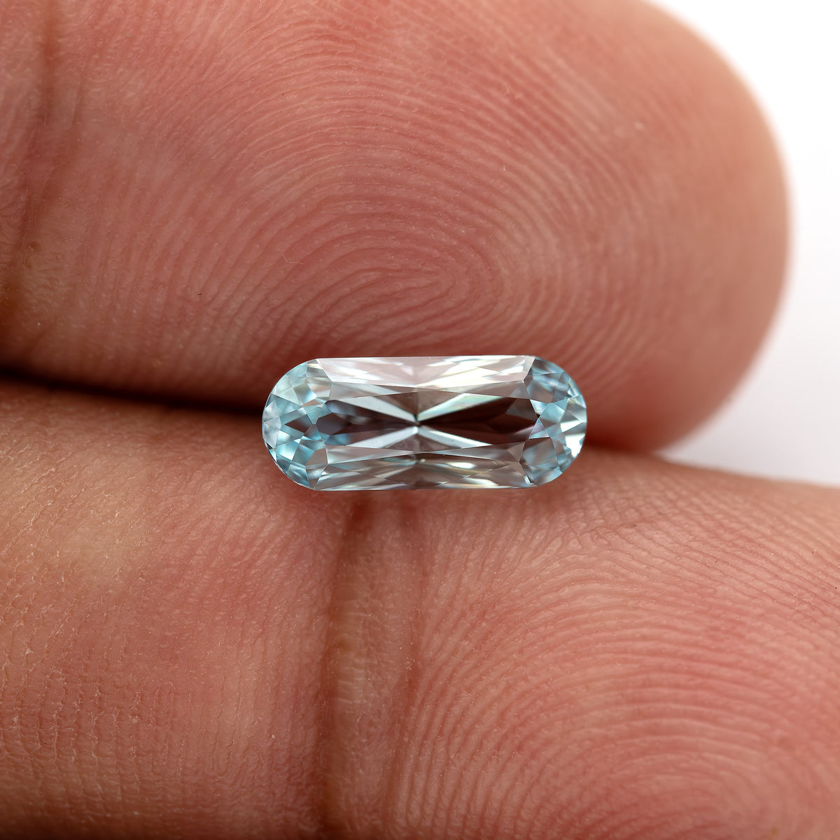 Wider fingertip view of the long-oval sapphire, showing its size against skin ridges.