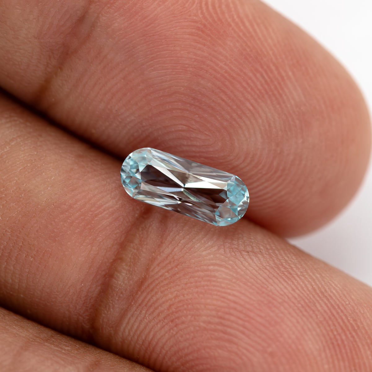 Light blue sapphire tilted on a fingertip, with bright central reflections.