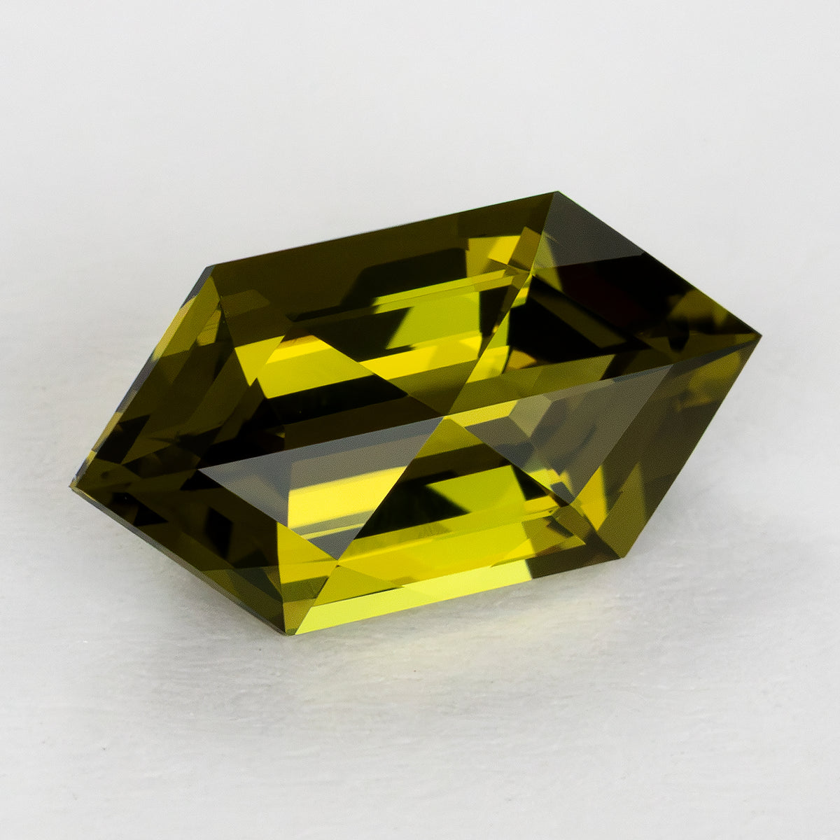 Yellow-green lab-grown sapphire in an angled crown view on a white surface, showing its elongated six-sided outline.