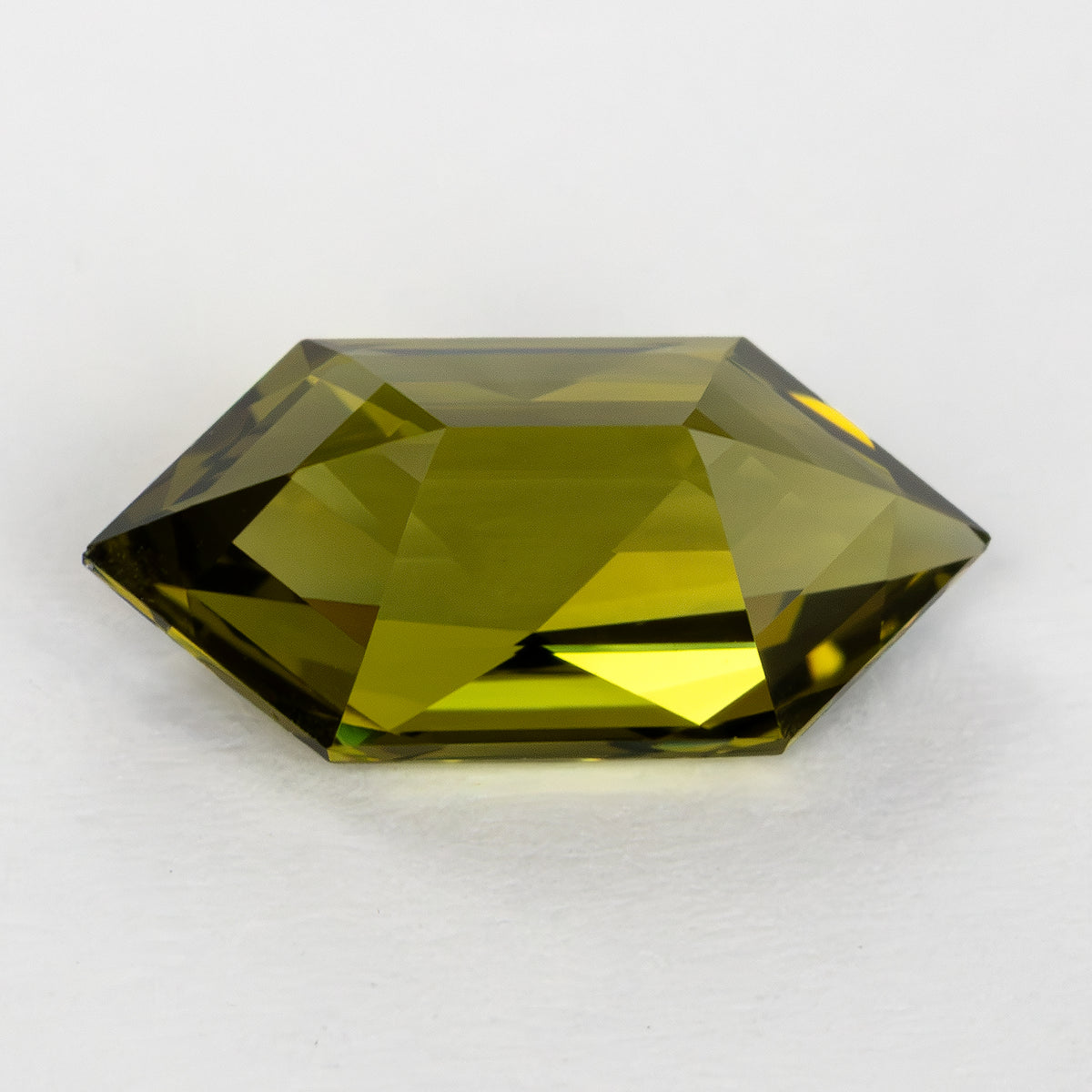 Low pavilion-side view of the yellow-green lab-grown sapphire on a white surface.