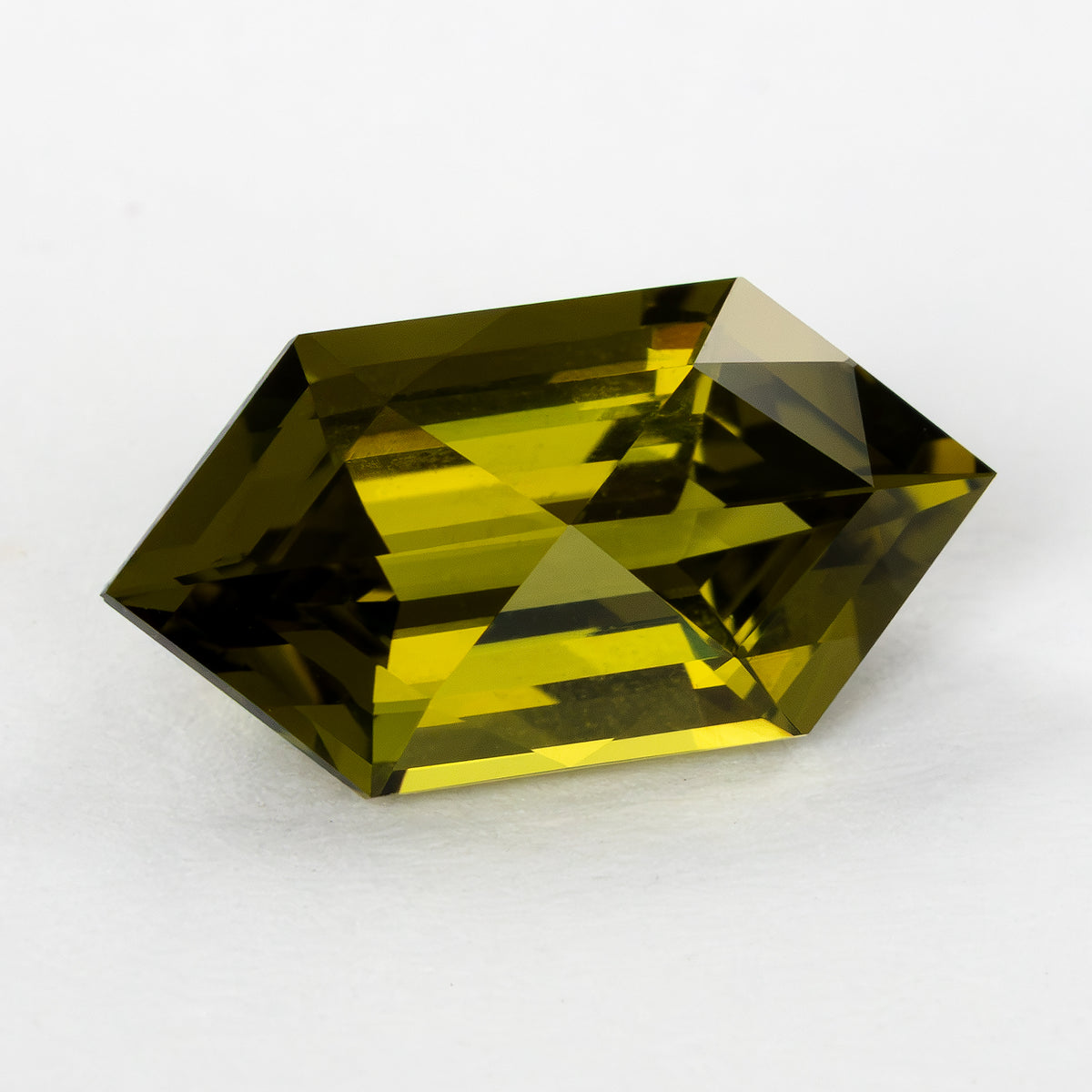 Elongated hexagonal lab-grown sapphire turned slightly on white, showing yellow and dark olive reflections.