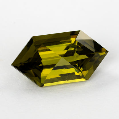 Elongated hexagonal lab-grown sapphire turned slightly on white, showing yellow and dark olive reflections.