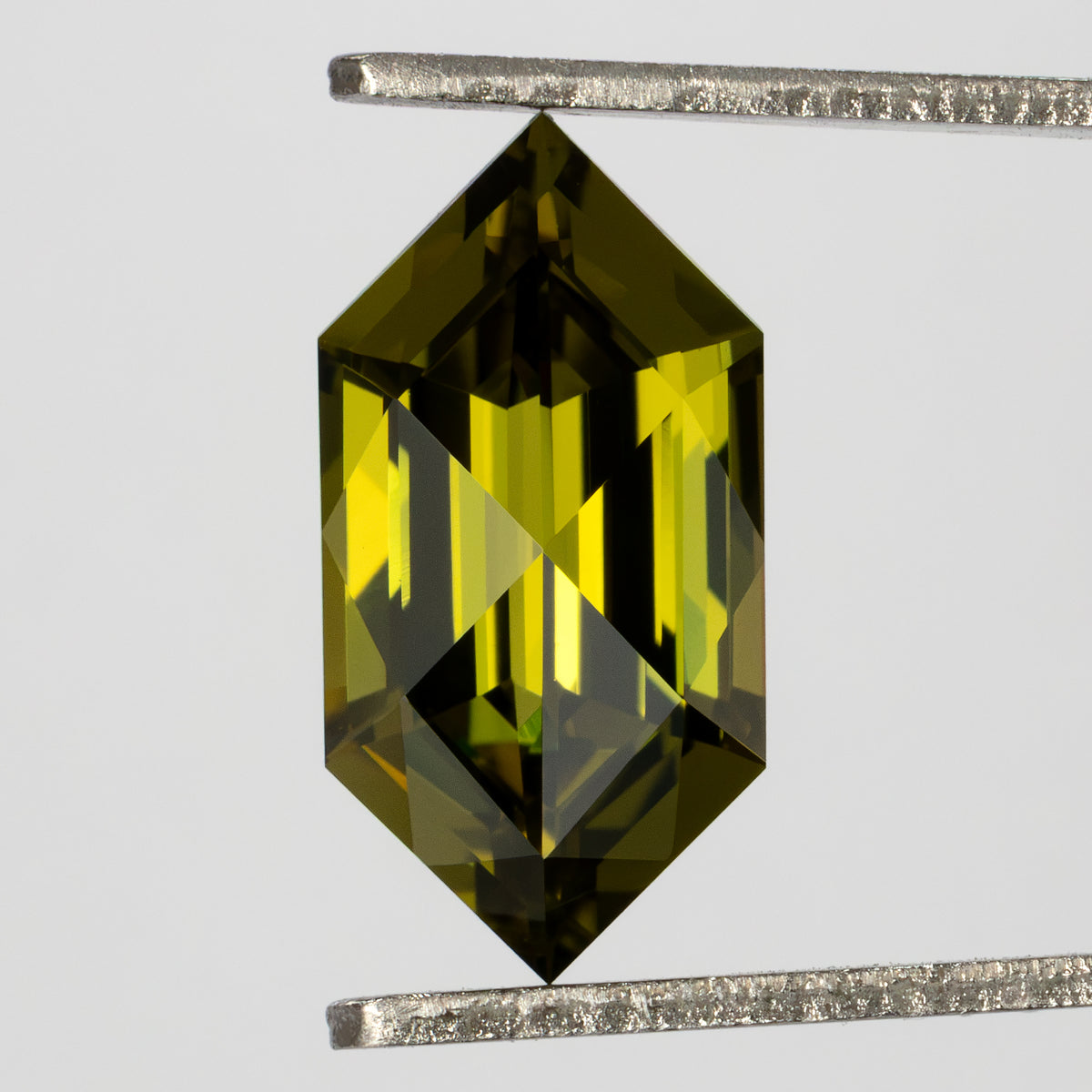 Face-up yellow-green lab-grown sapphire held vertically in tweezers, with pointed ends and long central facets.