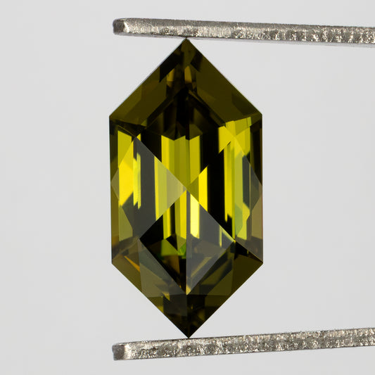 Face-up yellow-green lab-grown sapphire held vertically in tweezers, with pointed ends and long central facets.