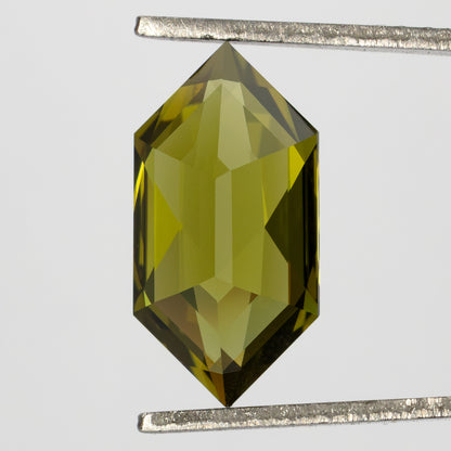 Back of the yellow-green lab-grown sapphire held vertically in tweezers, showing broad pavilion facets.