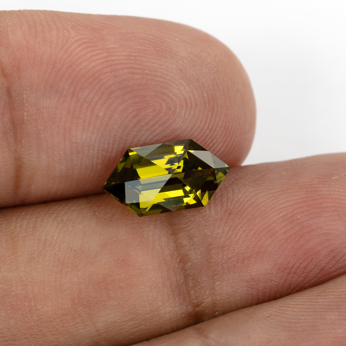 Yellow-green lab-grown sapphire resting across fingertips, with bright yellow and dark olive reflections.