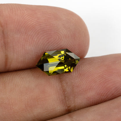Yellow-green lab-grown sapphire resting across fingertips, with bright yellow and dark olive reflections.