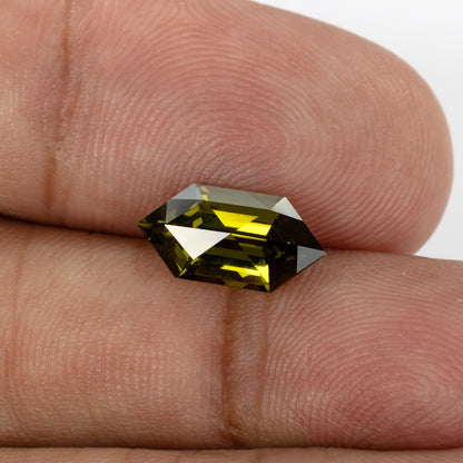 The elongated lab-grown sapphire on fingertips at a tilted angle, showing large bright facet reflections.