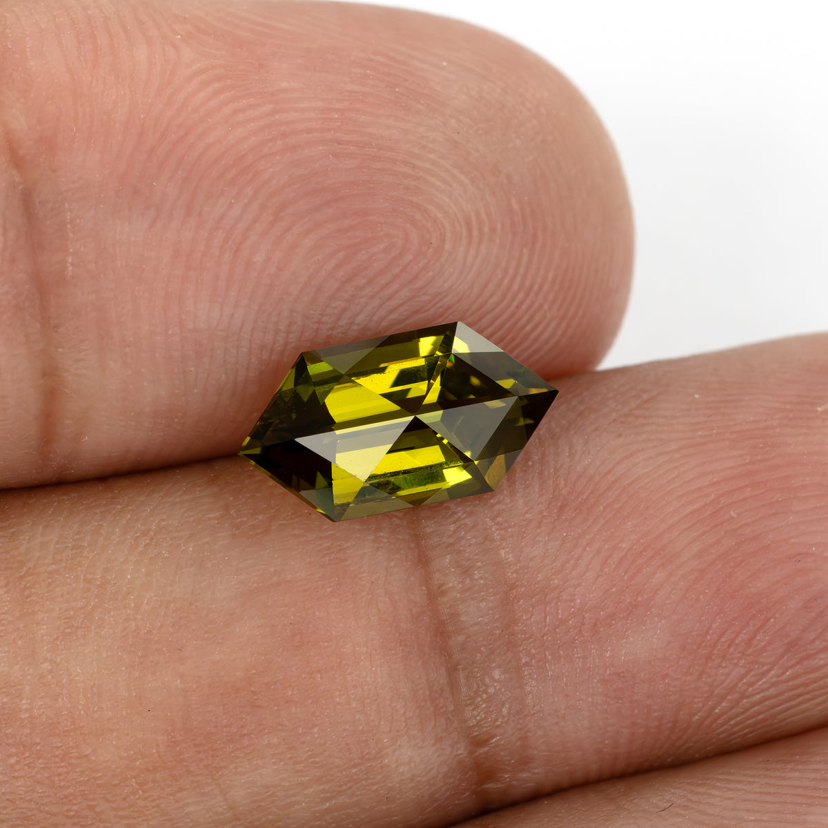 Yellow-green lab-grown sapphire on fingertips in another crown angle, showing its six-sided outline.