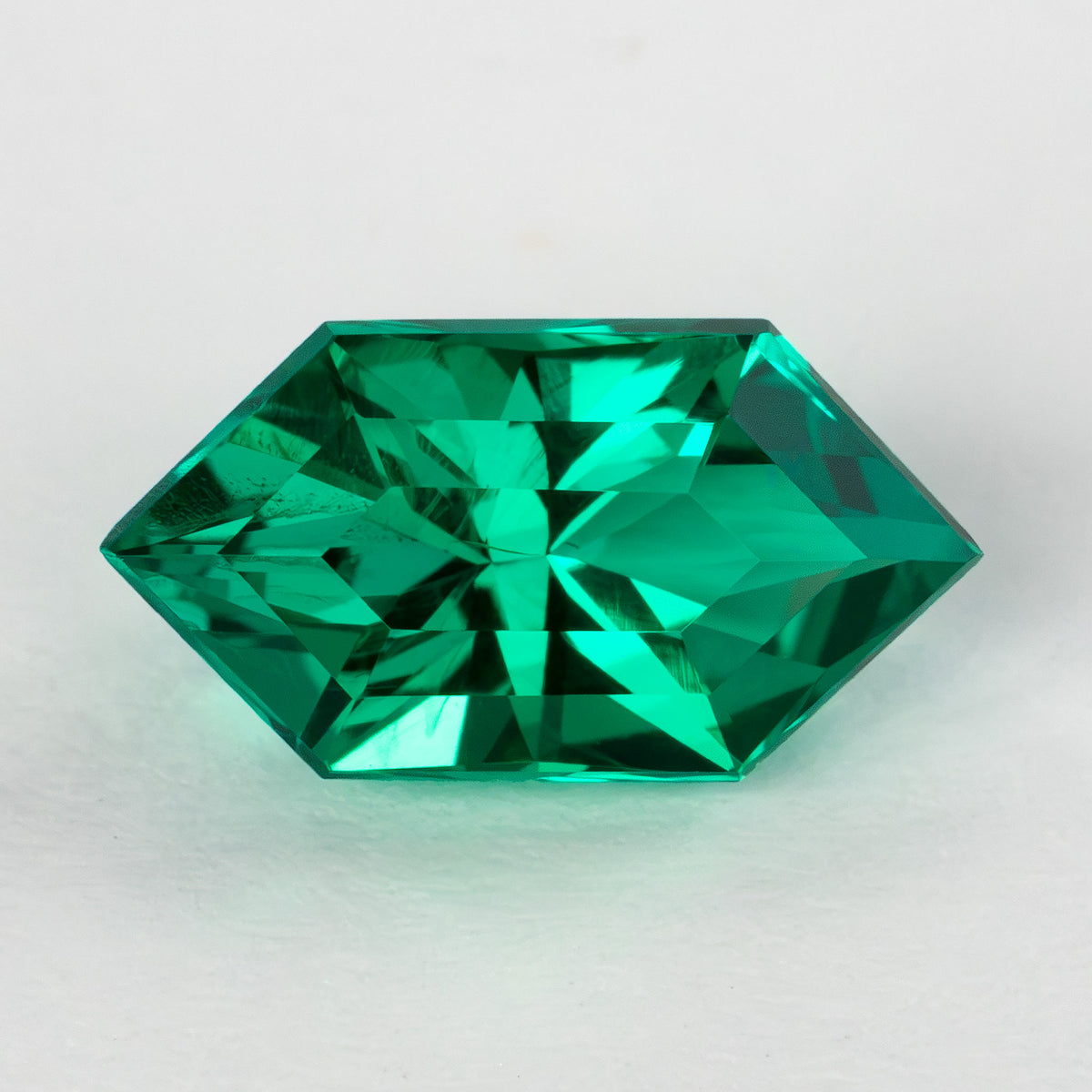 Green lab-grown emerald viewed horizontally from the crown on a white surface, showing its pointed ends.