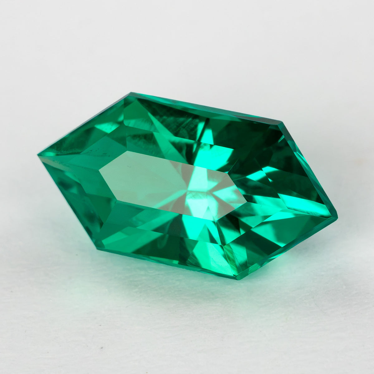 Green lab-grown emerald tilted on white, with broad pale and bright green crown reflections.