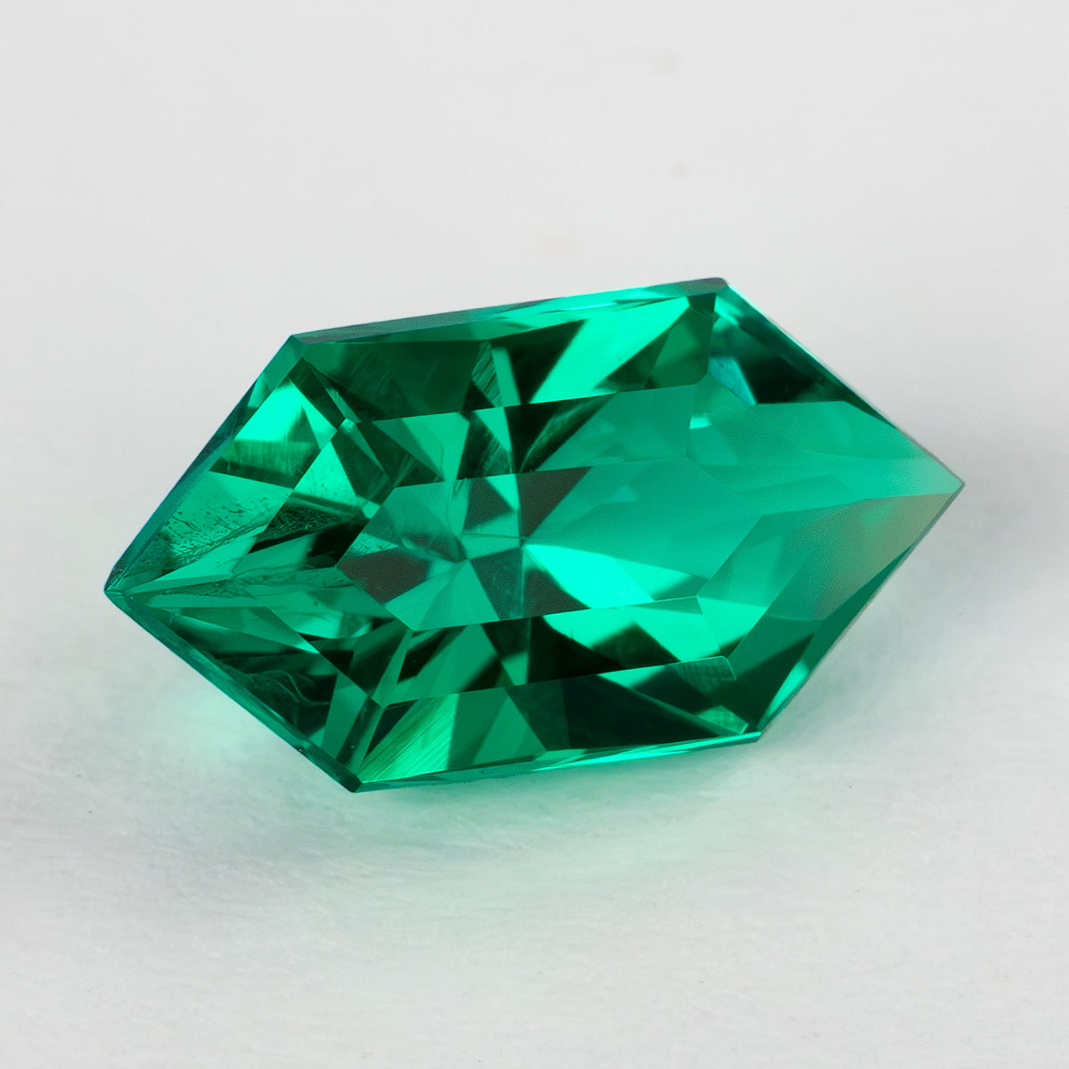 Elongated hexagonal lab-grown emerald at another crown angle, showing changing green facet reflections.