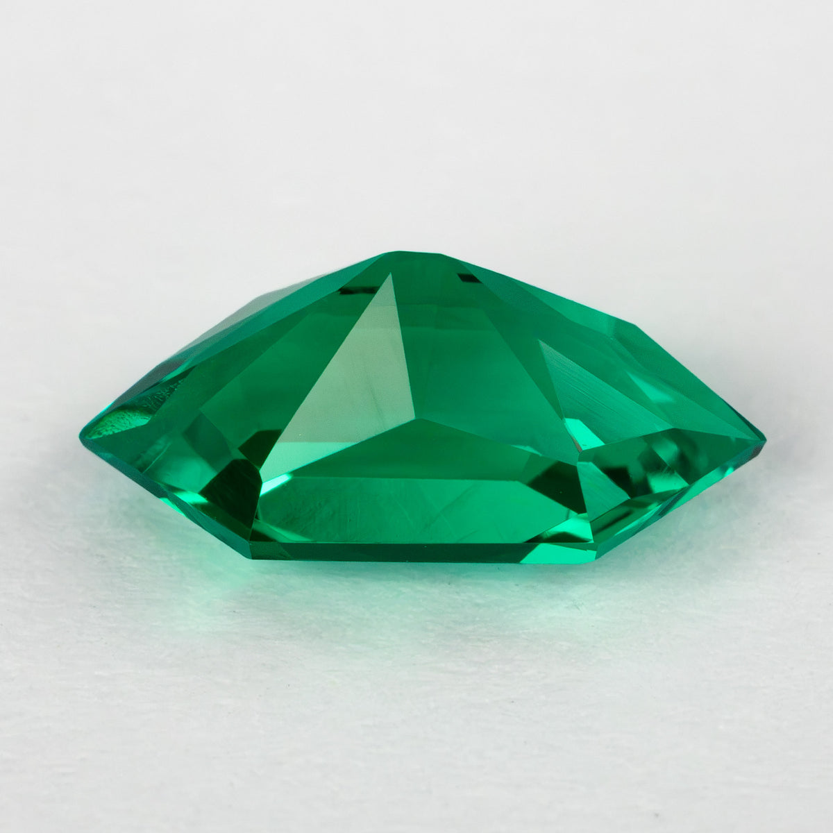 Low pavilion-side profile of the green lab-grown emerald on white, showing its depth and faceted back.