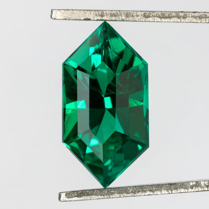 Face-up green lab-grown emerald held vertically in tweezers, showing its crown facets and fine visible internal features.