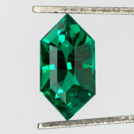 Face-up green lab-grown emerald held vertically in tweezers, showing its crown facets and fine visible internal features.