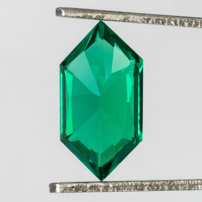 Back of the green lab-grown emerald held vertically in tweezers, showing broad pavilion facets.
