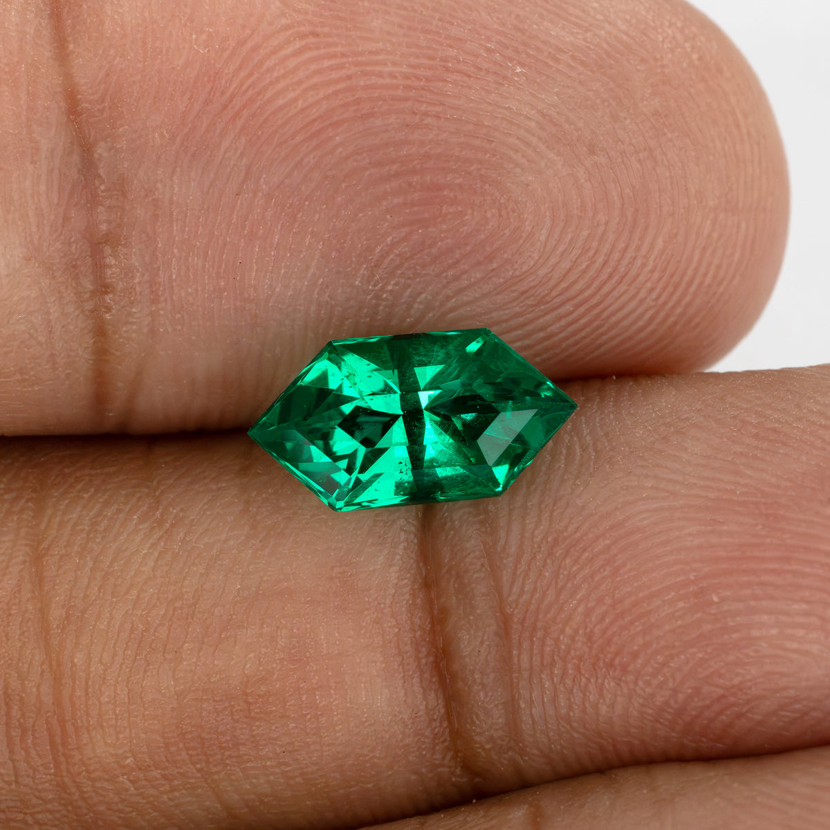 Green lab-grown emerald resting horizontally across fingertips to show its size and face-up appearance.