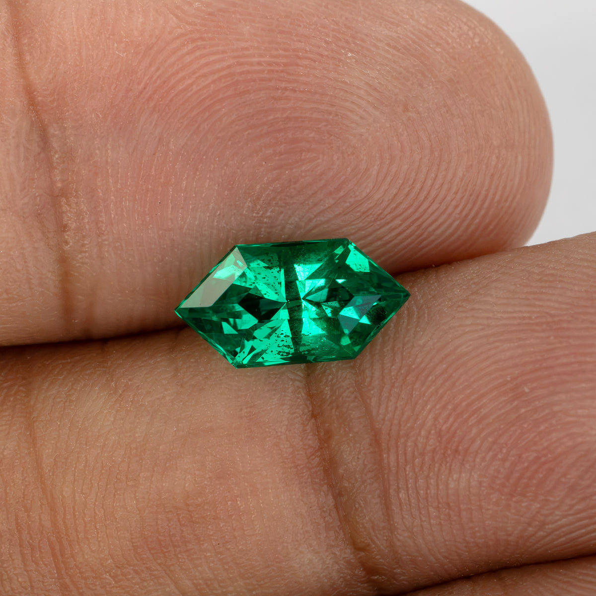 Green lab-grown emerald resting on fingertips in another crown view, showing pointed ends and darker reflections.