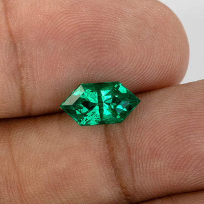 Green lab-grown emerald resting on fingertips in another crown view, showing pointed ends and darker reflections.