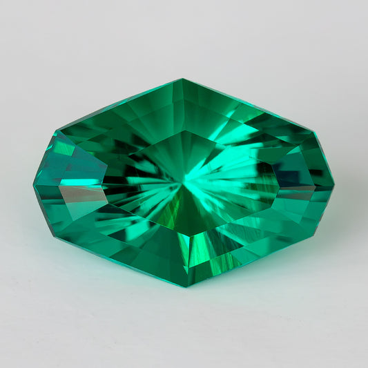 Face-up green octagonal lab-grown emerald on a white background, showing radiating central facets.