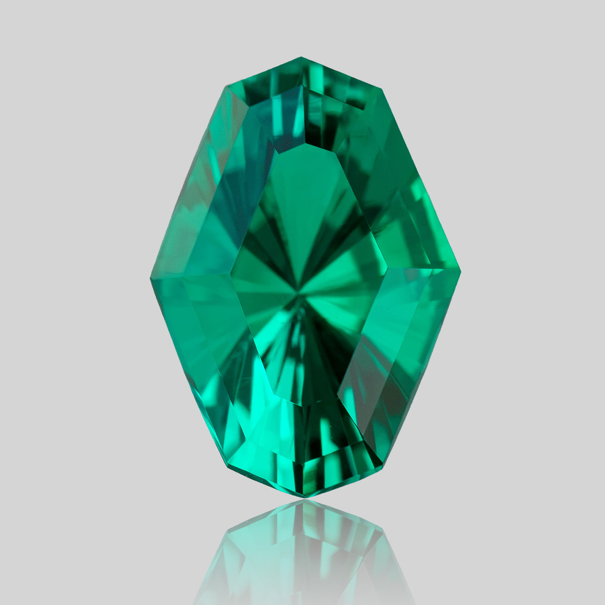 Green emerald standing upright on a reflective surface, with its face-up facet pattern visible.