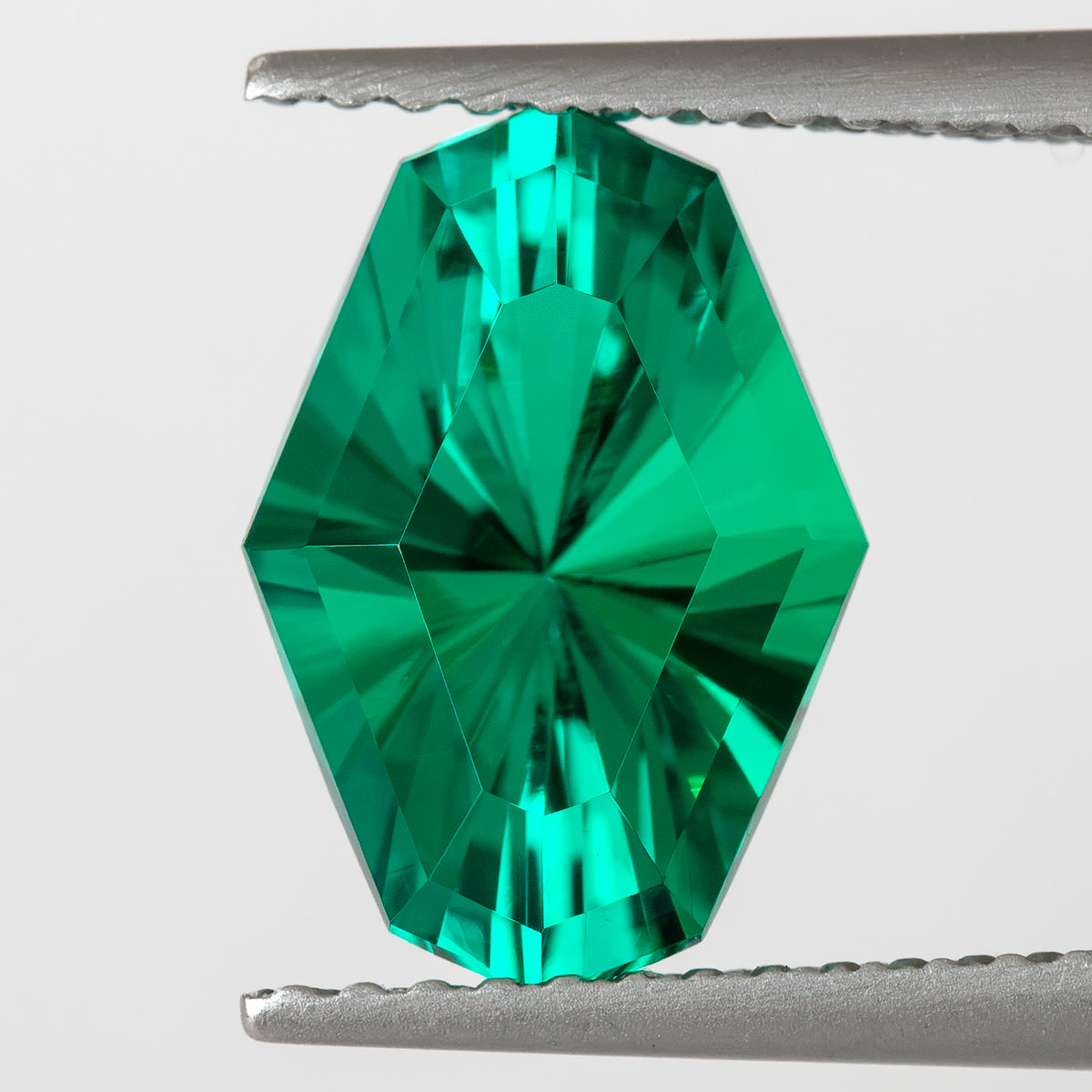 Face-up green octagonal emerald held vertically in tweezers, showing its full outline.
