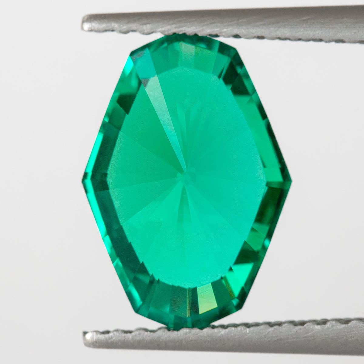 Reverse pavilion view of the green emerald held in tweezers, with a broad light central area.