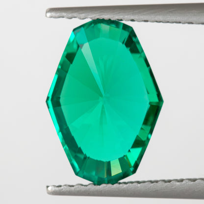 Reverse pavilion view of the green emerald held in tweezers, with a broad light central area.