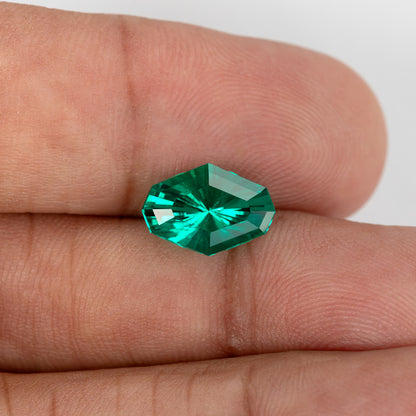Face-up emerald resting between fingers to show its size and green reflections.