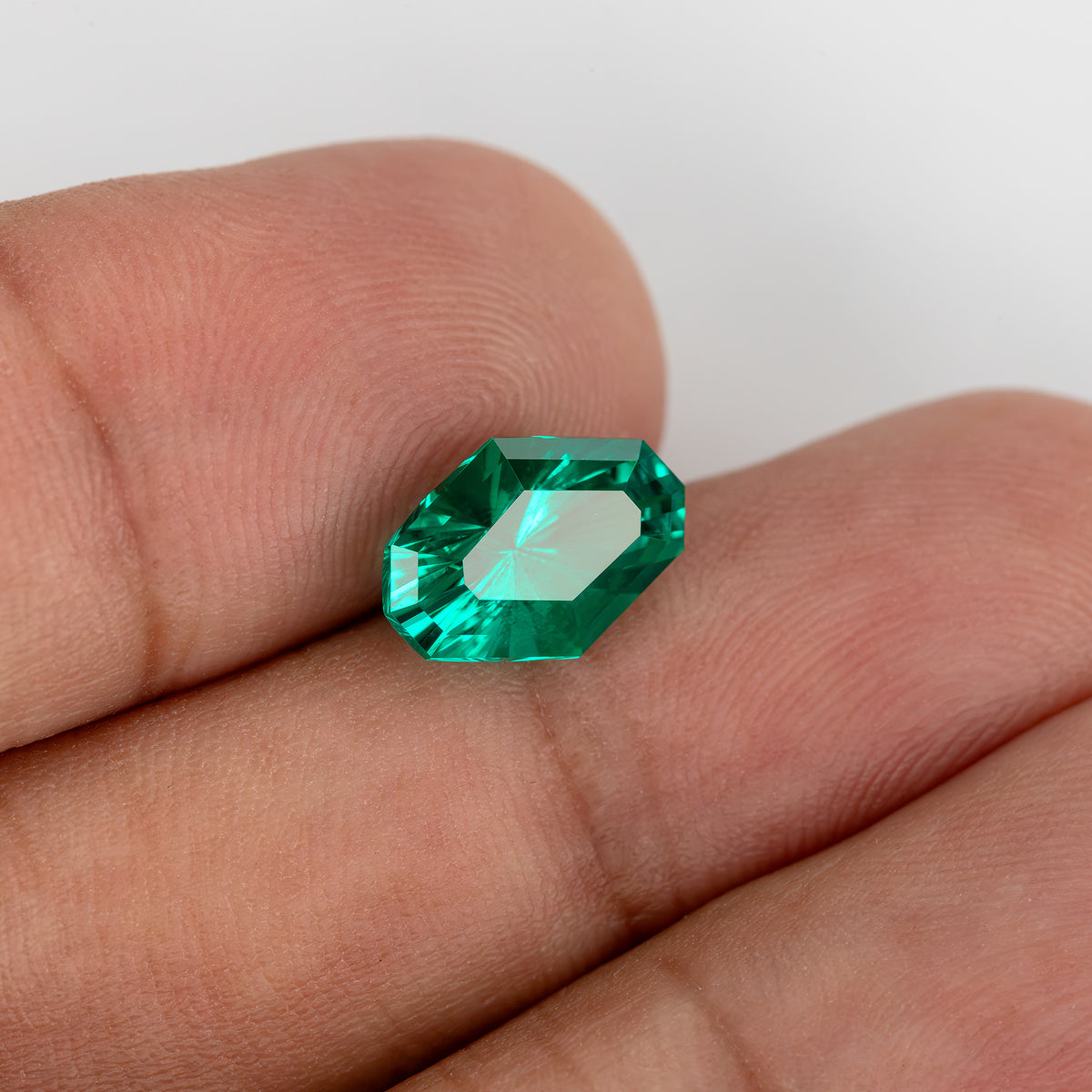 Tilted emerald on fingers with a broad bright reflection across its surface.