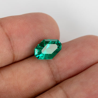Tilted emerald on fingers with a broad bright reflection across its surface.