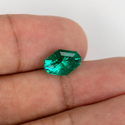 Oblique face-up emerald on fingers, showing its octagonal outline and radiating facets.