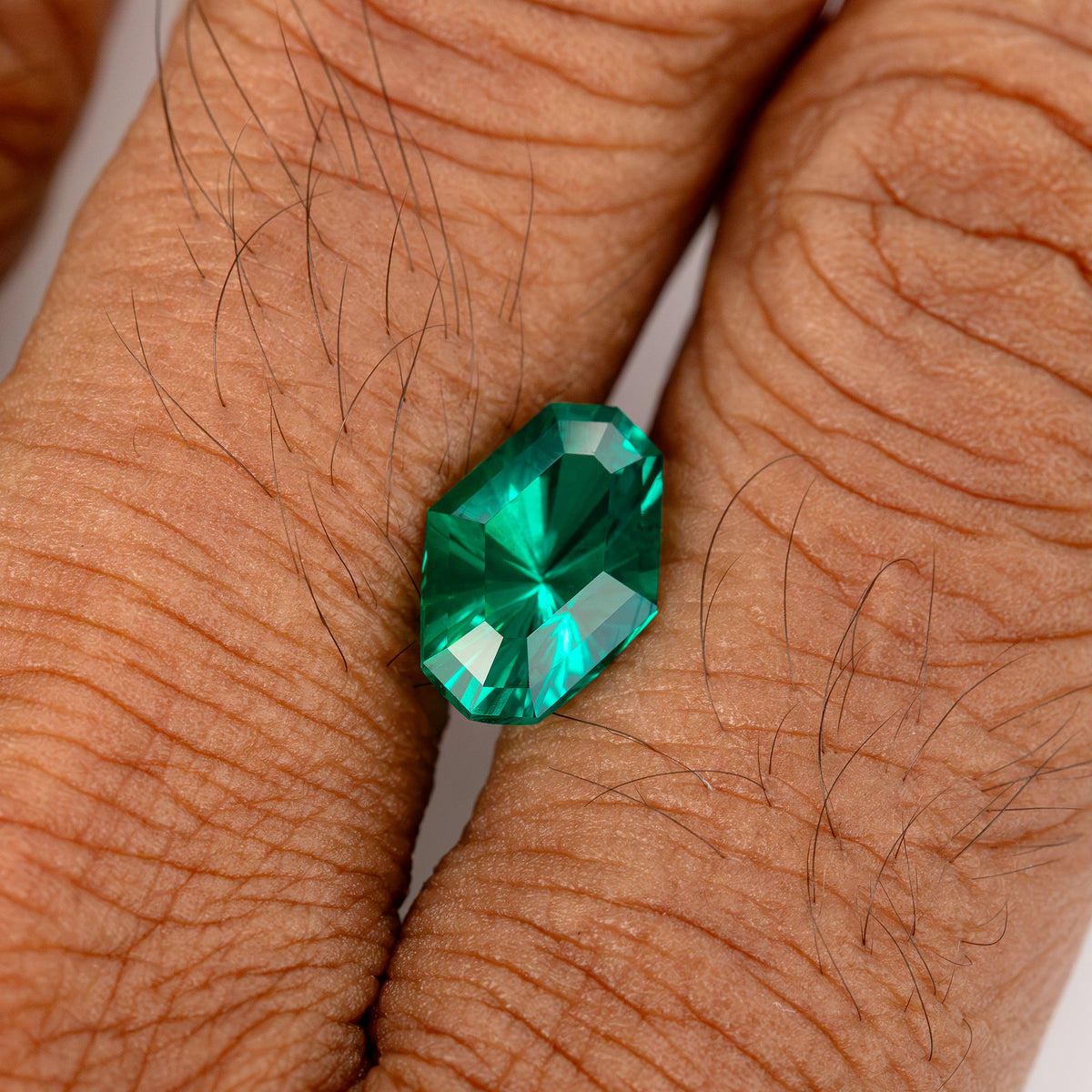 Green emerald resting on the back of a hand for scale.