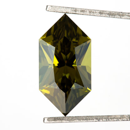 Long hexagonal yellow-green sapphire held upright in tweezers, with dark central reflections.
