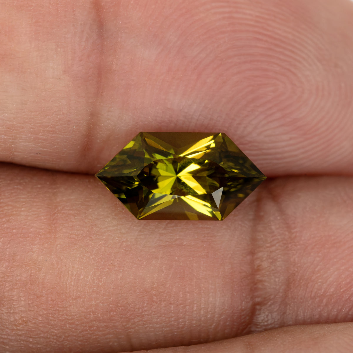 Face-up olive yellow-green sapphire resting on fingers, showing its size and long hexagonal outline.