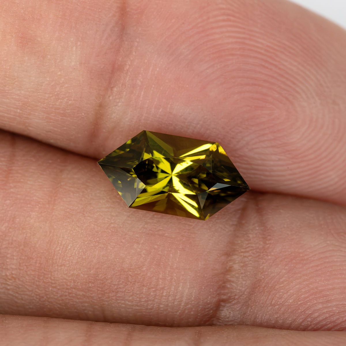 Oblique sapphire on fingers showing its side profile and green reflections.