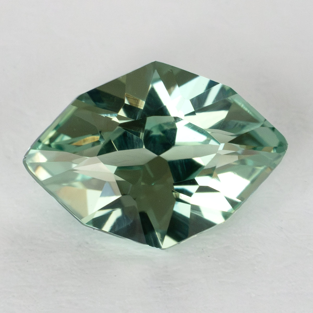 Pale green lab-grown sapphire viewed from the crown at a slight angle on a white surface.