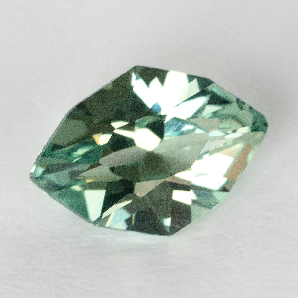 Lab-grown green sapphire tilted on a white surface, showing bright and dark crown reflections.