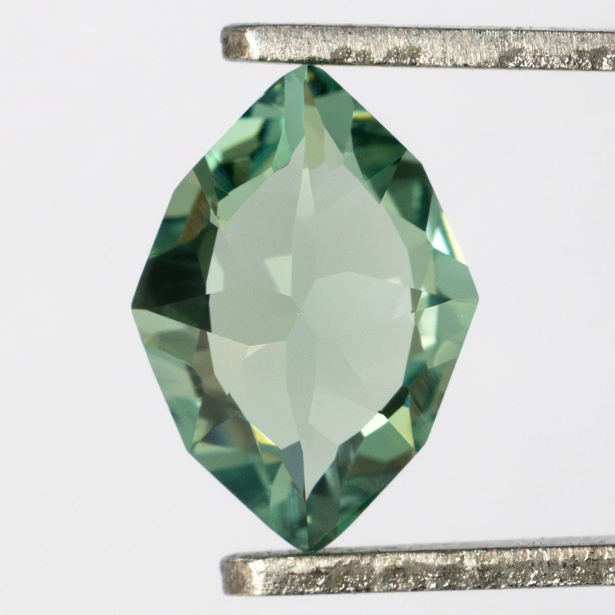 Back of the green lab-grown sapphire held vertically in tweezers, showing broad pavilion facets.