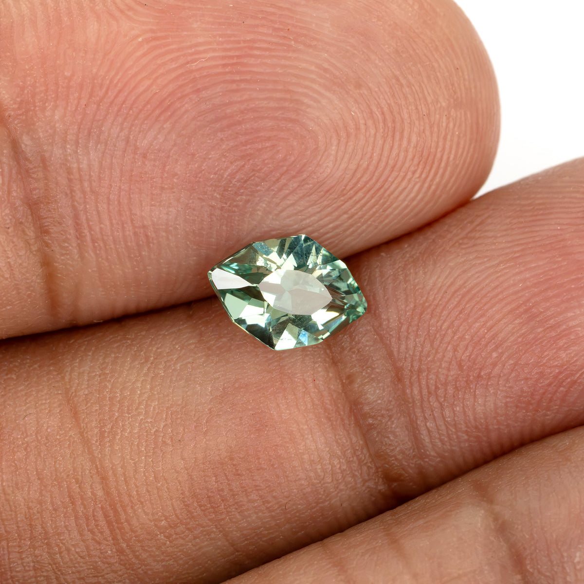 Green lab-grown sapphire resting across fingertips to show its size and face-up appearance.
