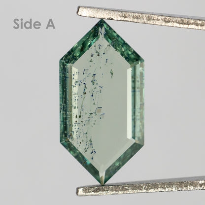 Elongated hexagonal green gemstone held vertically in tweezers labeled Side A, displaying fine internal inclusion trails.
