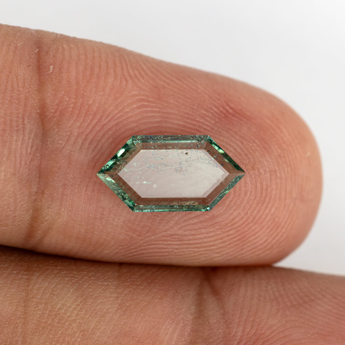 Elongated hexagonal green gemstone resting across adult fingertips for size perspective.