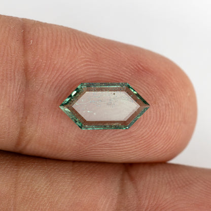 Elongated hexagonal green gemstone resting across adult fingertips for size perspective.