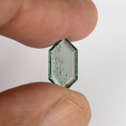 Elongated hexagonal green gemstone held upright between thumb and finger against neutral background.